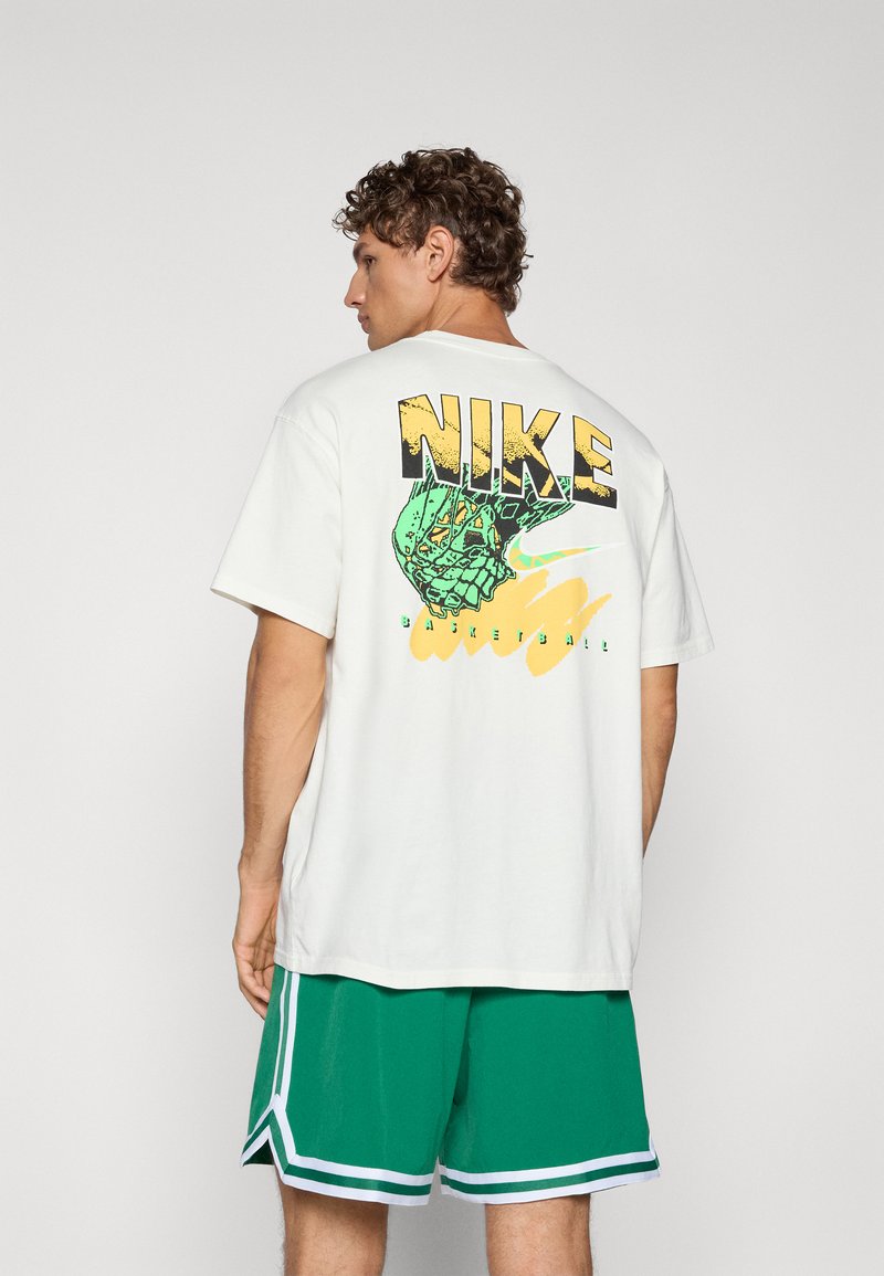 Witte katoenen T-shirt met een groen en gele grafische print op de rug, met de tekst "NIKE" en een basketbalontwerp. Draagt het met groene shorts.