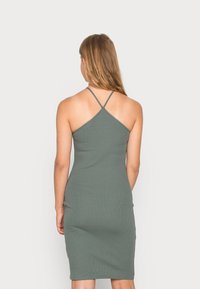 Vestido bodycon verde com nervuras, apresentando alças finas ajustáveis, uma silhueta ajustada e um corte até ao joelho, destacando uma textura suave.