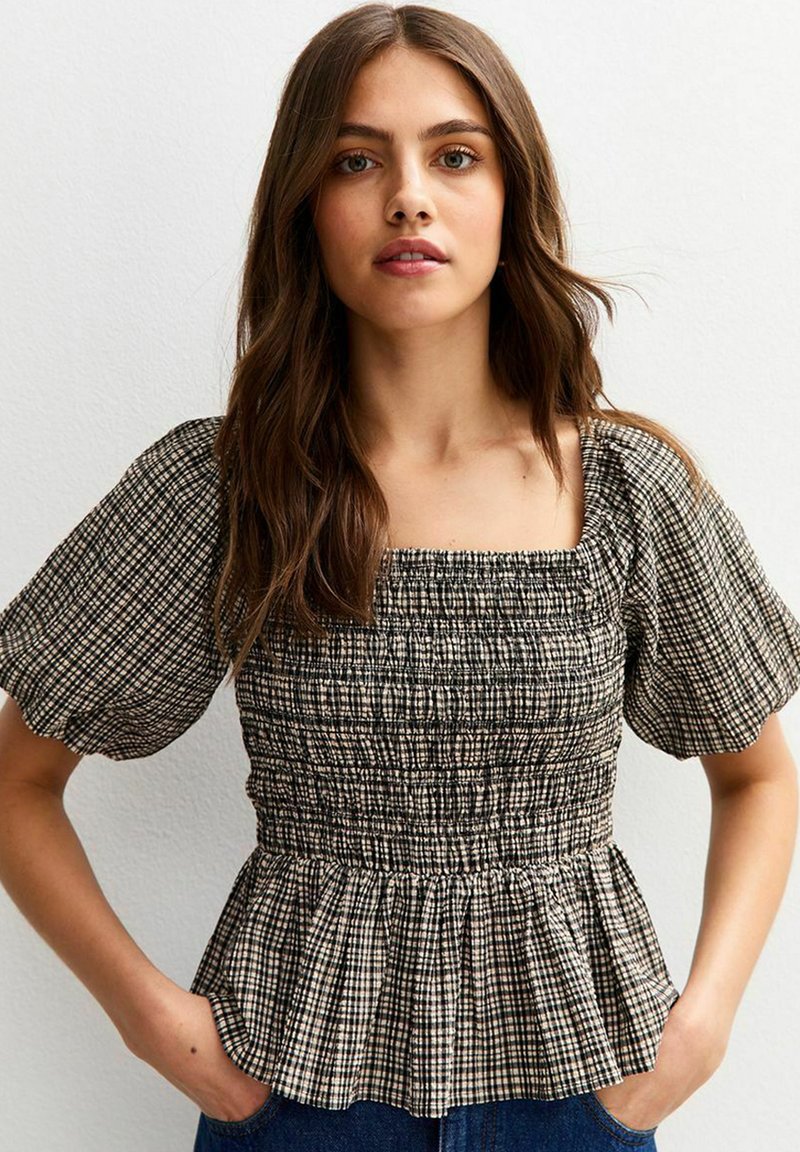 Blusa a cuadros en blanco y negro con smock, mangas cortas y con un bajo peplum. Presenta un escote cuadrado y una tela texturizada.