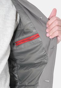 Interno della giacca grigia con una texture liscia, dotato di una tasca con zip rossa. La fodera è lucida e imbottita per l'isolamento.