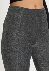 Zwarte en zilveren textuur leggings met een hoge tailleband, gemaakt van een glinsterend materiaal en een aansluitend ontwerp. Soepele oppervlakte met een lichte glans.