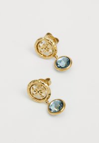 Boucles d'oreilles dorées présentant un design en découpe circulaire et une pierre bleue facettée suspendue en dessous. Le métal texturé ajoute un intérêt visuel.