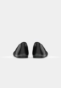 Črne usnjene čevlje z gladko površino, zaobljenim nosom, nizko peto in minimalističnim dizajnom. Imajo diskretno šivanje in slog za obuvanje.