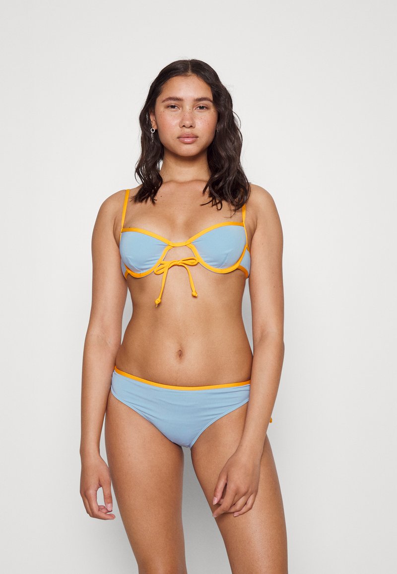 Conjunto de biquíni em tecido azul claro com detalhes laranja, desenhado com um laço ao centro e alças ajustáveis.