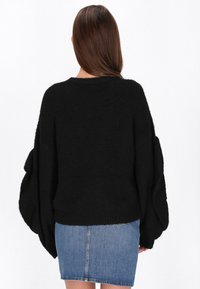 Czarny oversize sweter wykonany z miękkiego dzianiny, z długimi, luźnymi rękawami i ściągaczem u dołu. W połączeniu z dżinsową spódnicą.