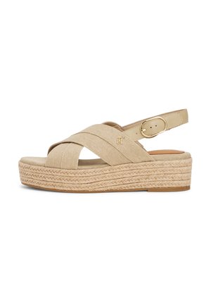 Beige espadrille-style sandal with cross-strap canvas upper, elastic heel strap, and woven jute platform sole. Gold-tone logo detail.