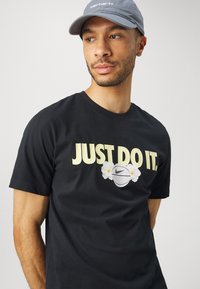 Svart bomull T-skjorte med teksten "JUST DO IT" i gult, et hvitt basketballmotiv med blomsterdetaljer, og en klassisk rundhalsdesign.