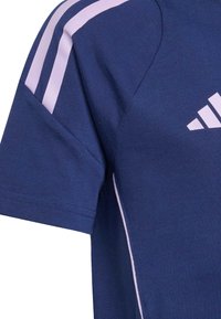Marineblå atletisk t-shirt med korte ærmer, der har hvide accentstriber på skuldrene og et hvidt logo på brystet. Lavet af struktureret stof.