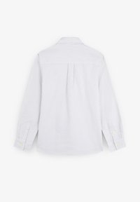 Camisa de manga larga con botones, con finas rayas verticales en gris y blanco, vista desde la parte posterior sobre un fondo blanco liso.