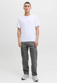 Hvit t-skjorte med rund hals kombinert med grå cargobukser med sidelommer. Brukt med grå treningssko på en ensfarget bakgrunn.