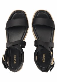 Czarne skórzane płaskie sandały z paskami na kostki, otwartymi palcami i plecionymi beżowymi podeszwami, z logo Michael Kors na wkładkach.