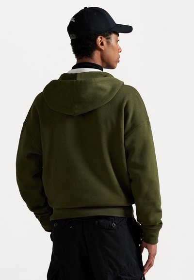 Olive green sweatshirt with a hood, soft texture, dropped shoulders, and black accents. Worn with black cargo pants.