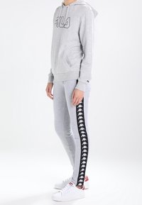 Grå sweatshirt med huva och framficka, med en svart logo. Grå leggings med svart sidrand och vita logodetaljer. Vita sneakers.