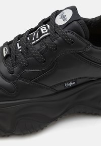 Black sneaker made of smooth leather with textured sole. Features thick laces, logo tag on the tongue, and streamlined silhouette.