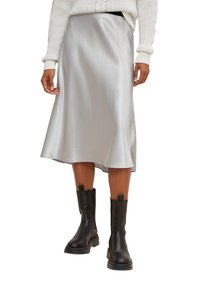 Falda midi de satén plateada con una suave forma de A, que presenta una textura suave y una abertura lateral, combinada con botas negras hasta el tobillo.
