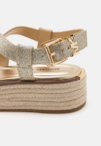 Gold glitter strap sandals with a chunky woven jute platform. Features a gold buckle and logo on the insole for added detail.