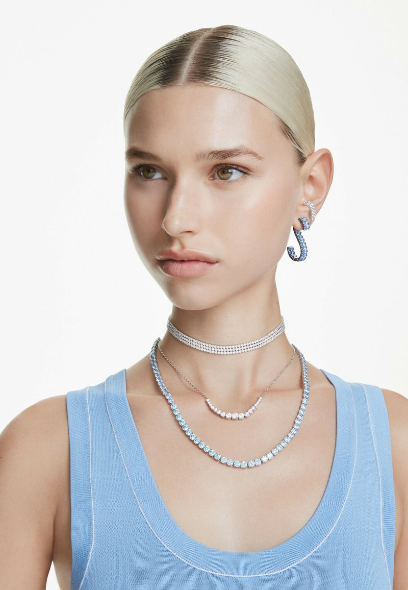 Smycken i silver och blått har ett chokerhalsband, lager av halsband och en hoop-örhänge. Texturerad tygtopp i ljusblått.