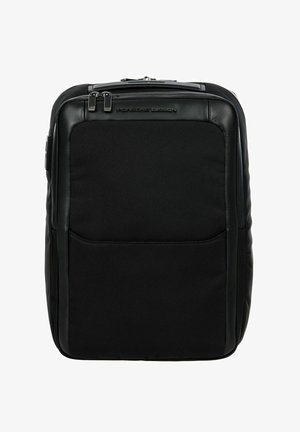 Mochila negra que presenta una combinación de materiales sintéticos lisos y texturizados, cierre con cremallera y un bolsillo frontal. Diseño compacto y rectangular.