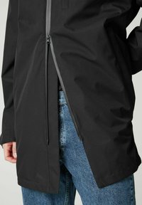 Schwarze wasserdichte Jacke mit durchgehendem Reißverschluss, taillierter Passform und hohem Kragen; verfügt über eine geschlitzte Saum und kontrastierende Reißverschlussdetails.