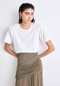 T-shirt bianco a maniche corte in cotone, abbinato a una gonna taupe arricciata con un design fluido. Stile semplice e classico.