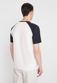 Camiseta de hombre con mangas raglán en azul marino y cuerpo blanco, hecha de algodón suave, con cuello redondo y dobladillo recto.