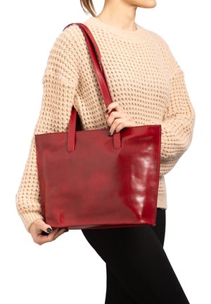 Borsa tote rossa in pelle con finitura lucida, forma rettangolare e manici per spalla, tenuta da una persona con un maglione lavorato a maglia color beige.