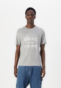 Gray cotton t-shirt featuring a rounded neckline and front print in white text. Worn with loose blue denim shorts.