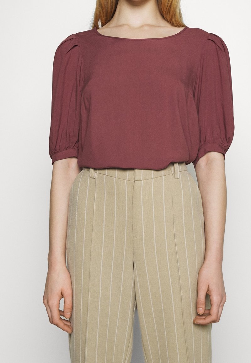 Bordowa bluzka z krótkim rękawem i kwadratowym dekoltem, z marszczonymi bufkami na rękawach. Połączona z beżowymi, wąsko prążkowanymi spodnie z wysokim stanem.