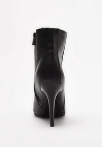 Bottine en cuir noir à finition lisse, talon stiletto haut, et détail de fermeture éclair latérale. Caractérisée par une silhouette ajustée et un bout effilé.