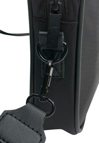 Róg czarnej torby materiałowej z zamkiem błyskawicznym i metalowym złączem, z teksturowanym skórzanym paskiem i okrągłym pierścieniem do zawieszenia.