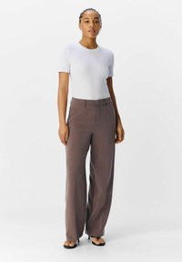 T-shirt blanc ajusté associé à un pantalon large à rayures brunes taille haute. La tenue présente un design épuré avec des accents minimaux.
