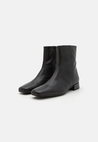 Botines de cuero negro con un acabado suave, puntera cuadrada y cremallera lateral. El bajo tacón en bloque y el diseño sin costuras crean una silueta elegante.