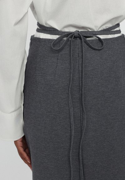 Sudadera gris con un cinturón atado en la cintura, hecha de un tejido suave con una textura lisa, combinada con una camisa blanca de cuello.