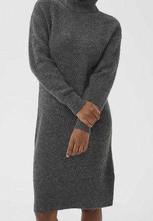 Personne portant une robe en tricot côtelé gris foncé à col roulé avec des manches longues, les mains croisées aux poignets devant.