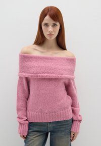 Rosa Off-Shoulder-Pullover aus weichem, strukturiertem Strickstoff. Gerippter Saum und Ärmelabschlüsse. Kombiniert mit hellblauen Jeans.