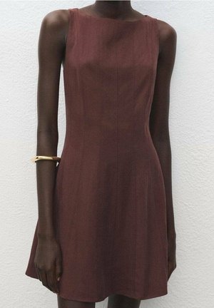 Robe marron foncé sans manches, longueur au genou, portée par une personne à la peau foncée, portant un bracelet manchette doré sur le haut du bras gauche.