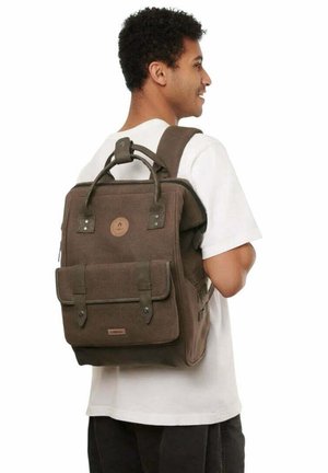 Brauner Canvas-Rucksack mit einem oberen Tragegriff, Frontklappen-Tasche und verstellbaren Schulterriemen. Mit Logo-Patch und Metallakzenten.