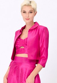 Veste cropped en satin rose avec un col pointu, des manches trois-quarts et une texture lisse. Portée sur un ensemble coordonné de haut et de jupe.