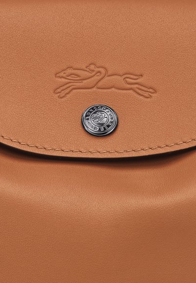 Tasche aus braunem Leder mit geprägtem laufenden Pferdelogo und rundem Metallknopf, der mit "Longchamp 1948" graviert ist.