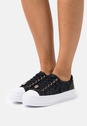 Schwarze Schnürsneaker mit flacher weißer Sohle, strukturiertem schwarzen Obermaterial, runder Zehenpartie und dekorativen Metallakzenten an den Schnürsenkeln.