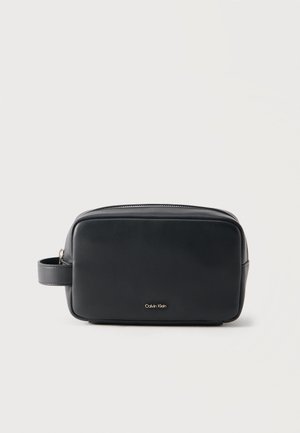 Schwarze rechteckige Kulturtasche aus Leder mit seitlichem Griff und Reißverschluss, kleines goldenes Calvin Klein Logo in der Mitte vorne.