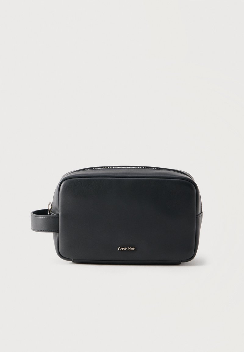 Μαύρο ορθογώνιο δερμάτινο τσαντάκι καλλυντικών με πλευρική λαβή και φερμουάρ, μικρό χρυσό λογότυπο Calvin Klein στο κέντρο της μπροστινής πλευράς.