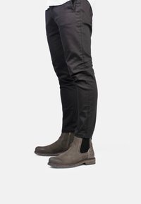 Botas Chelsea de cuero marrón con cremalleras laterales, acabado texturizado, suelas de goma, usadas con pantalones negros ajustados.