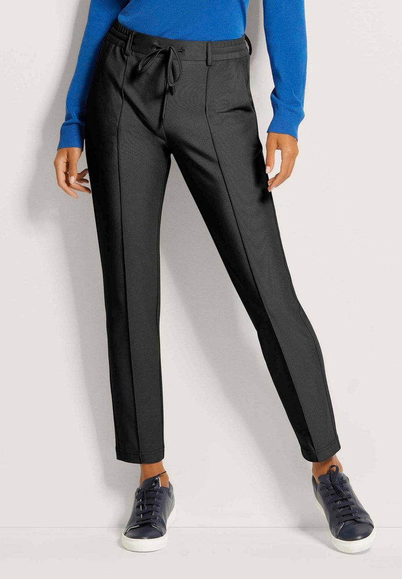 Zwarte, op maat gemaakte broek met een trekkoord in de band en zijstrepen. Gladde textuur, getailleerd ontwerp, gecombineerd met marineblauwe sneakers.