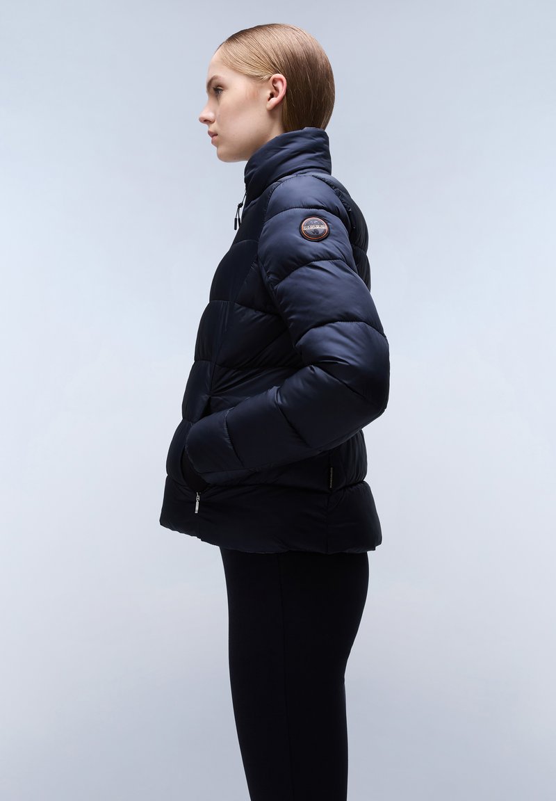 Giubbotto imbottito blu navy con colletto alto, texture trapuntata, tasche laterali e patch del logo sul braccio sinistro. Chiusura con zip frontale.