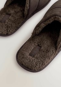 Mørkebrune hjemmesko med en blød, fuzzy inderside og en glat yderside. Designet har en struktureret overdel og en holdbar sål.