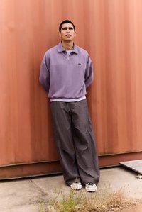 Lilla fleecejakke med glidelås og høy krage, sammen med grå bukser med løs passform. Hvite joggesko med svarte og fargede detaljer. Glatte teksturer.