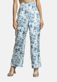 Pantalons larges blancs avec un motif floral bleu, dotés d'une taille haute et d'un tissu léger et doux. Associés à des talons fins argentés.