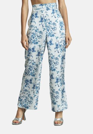 Weiße weit geschnittene Hosen mit einem blauen Blumendruck, mit hoher Taille und einem glatten, leichten Stoff. Kombiniert mit silbernen, schmalen Absatzschuhen.