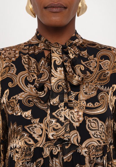 Rochie neagră cu un model paisley auriu, cu un guler tip fundă, mâneci lungi și o textură fluidă.